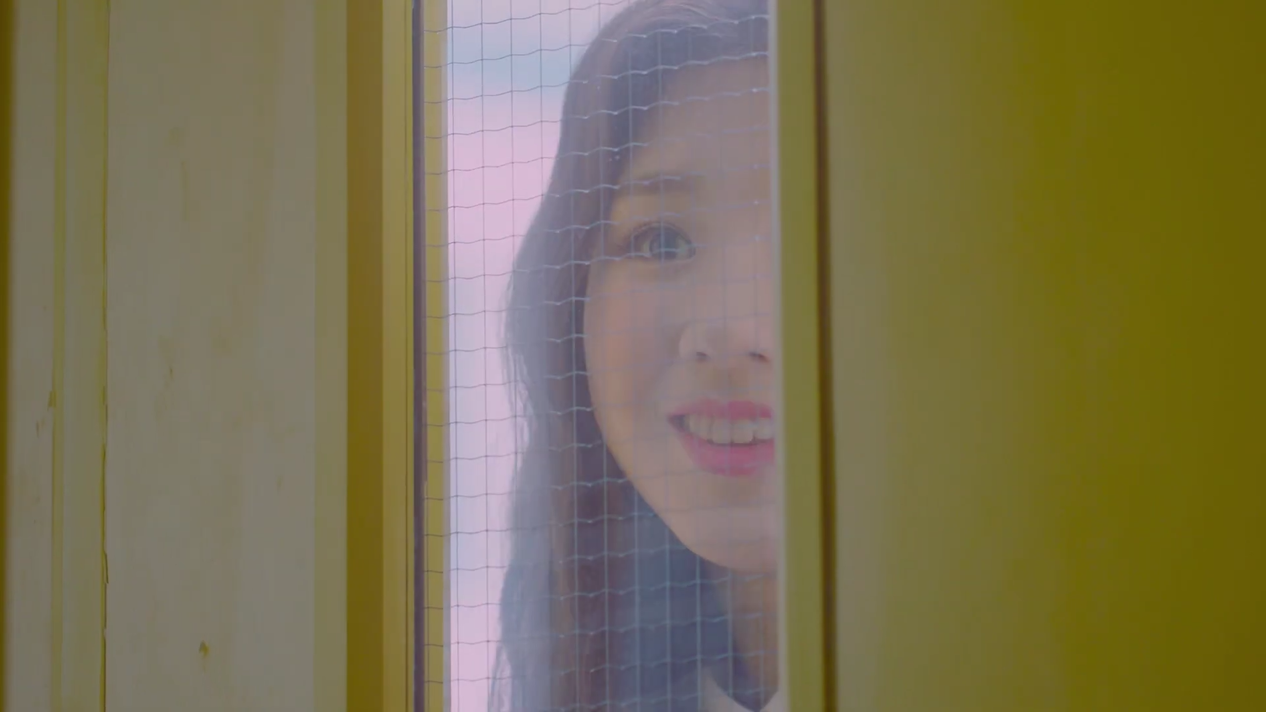 Heejin smiling through the window of a door.